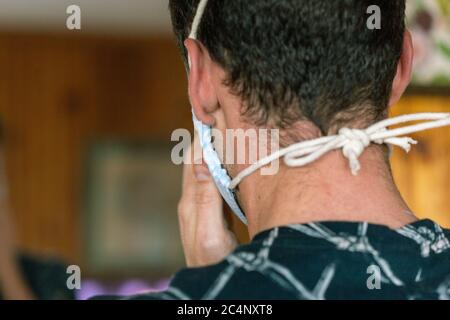 Junge männliche Anziehen Deluxe Stoff Maske Seite muskulösen jungen Mann in dunkel gemusterten Hemd auf hellem Holz Hintergrund Stockfoto