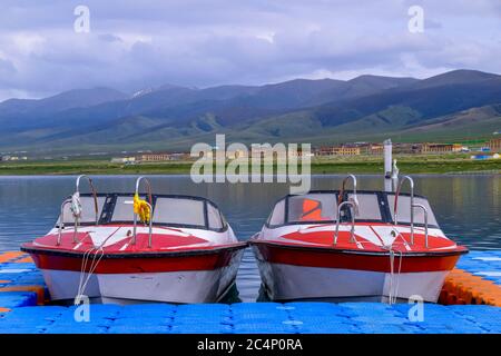 Die weite Landschaft des Qinghai Sees, sowie mehrere Kreuzfahrtschiffe und Yachten, die am See angedockt sind, der blaue Himmel und weiße Wolken, herrlich und bewegend Stockfoto