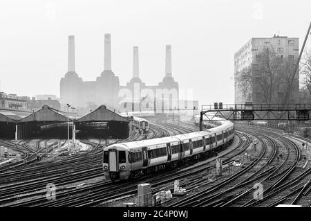 Bewegen Nahverkehrszüge und Bahnstrecken in London, mit Battersea Power Station hinter dem Nebel im Hintergrund erkannt zu werden. Schwarz und Weiß. Stockfoto