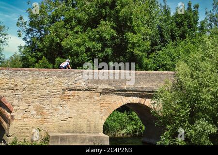 Ein Radfahrer in Lycra auf der alten Dorfbrücke über den Fluss Great Ouse in Harrold, England, Bedfordshire, Großbritannien Stockfoto