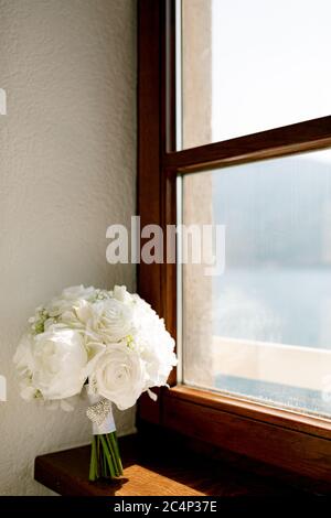 brautstrauß aus reinen weißen Rosen, Babyluft, weißen Bändern und Brosche am Fenster Stockfoto