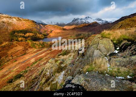 Ultra Wide View Of Dramatic Landscape Blea Tarn With Snow On Langdale Pikes And Dark Moody Clouds. Lake District, Großbritannien. Stockfoto