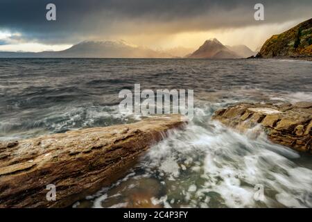 Dunkle Und Moody Wolken Mit Regenschauern, Die Über Die Schottischen Highland Mountains Fahren Und Wellen Über Rocks On Shoreline Krachen. Elgol, Isle of Skye, Großbritannien. Stockfoto