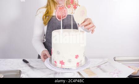 Einfügen von großen Lutscher mit Schneeflocken in den hohen Weiße, runde Kuchen als Dekoration. Stockfoto