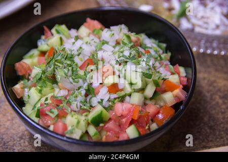 Frischer israelischer Gemüsesalat mit Gurke, Tomaten, weißen Zwiebeln und Petersilie, serviert in einer dunklen Schüssel Stockfoto
