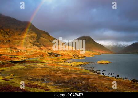 Regenbogen in EINER dramatischen Landschaft mit abendlichen goldenen Licht auf den Bergen und dramatischen Wolken über dem See. Wastwater, Lake District, Großbritannien. Stockfoto