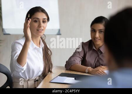 Lächelnde arabische Geschäftsfrau, die Hand hebt und Frage an Mentor stellt Stockfoto