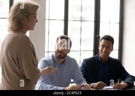 Verschiedene Kollegen hören beim Briefing dem reifen Business Coach zu Stockfoto