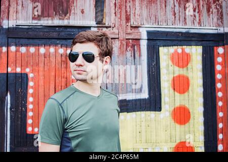 Mann in Sonnenbrille, der in der Ferne gegen die bemalte Holzwand schaut Stockfoto