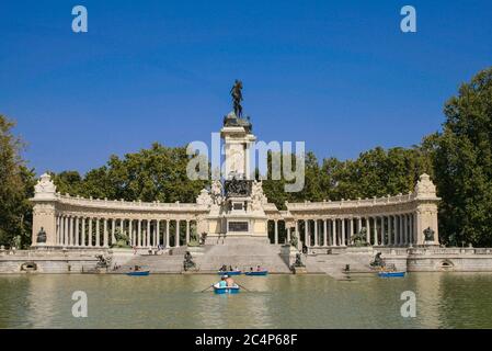 Madrid, Comunidad de Madrid, Spanien, Europa.. El Retiro Park (Parque del Retiro). Pannoramischer Blick auf den See und die Statue von König Alfonso XII, die Teil einer Gruppe ist, die aus einer großen Marmorkolonnade mit zahlreichen Skulpturen besteht, die die Bronzestatue des Königs umgeben. Das Denkmal, wurde am 6. Juni 1922 eingeweiht und vom Architekten José Grases Riera erbaut. Stockfoto