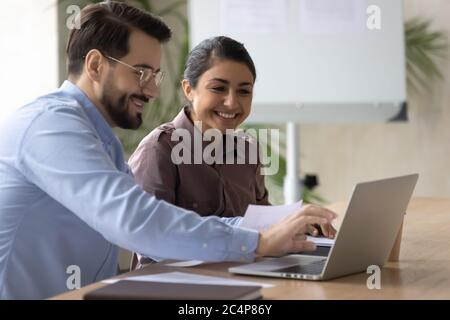 Lächelnde Kollegen, die gemeinsam mit einem Laptop an einem Projekt arbeiten Stockfoto