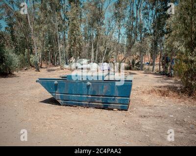 Große blaue Metallmülltonne auf einem Campingplatz im Jordantal Israels. Viele Zelte in der Nähe der Eukalyptusbäume im Hintergrund. Abenteuerurlaubse Stockfoto