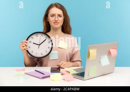 Überstunden. Erschöpft ermüdet verärgert Frau Angestellter in Brillen sitzen am Arbeitsplatz Büro, alle mit Haftnotizen bedeckt und hält große Uhr. Stockfoto