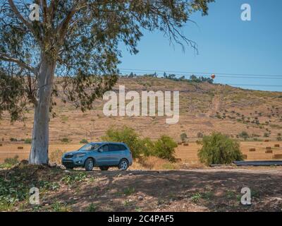 Graues Geländewagen Geländewagen unter einem Eukalyptus-Baum Schatten auf einer unbefestigten Straße geparkt. Die Landschaft der Berge und Weizenfelder mit Heuballen im Grafen Stockfoto