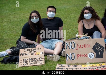 Drei junge Leute saßen im Park bei der Versammlung der BLM-Demonstranten in Canterbury; mit ihren Plakaten und Gesichtsmasken. Stockfoto