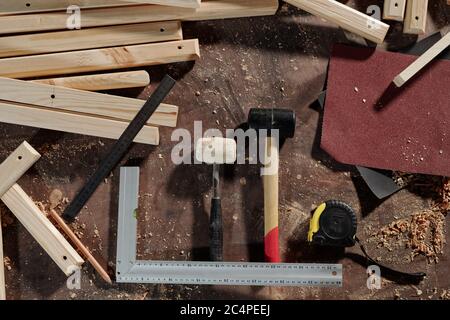 Oben Ansicht von Zimmermannswerkzeugen wie Hämmer, Maßband, Schleifpapier, Lineale und Bleistiftplätze auf dem Schreibtisch mit Holzbohlen und Späne Stockfoto