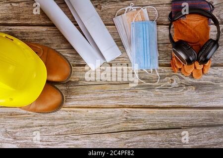 Industrie Arbeiter Schutz-und OP-Maske, Ohrenschützer Arbeitskleidung Sicherheitsstiefel Leder Handschuhe gelb Hut auf Architekten arbeiten mit Blaupausen im Büro coronavirus Pandemie covid-19, Stockfoto