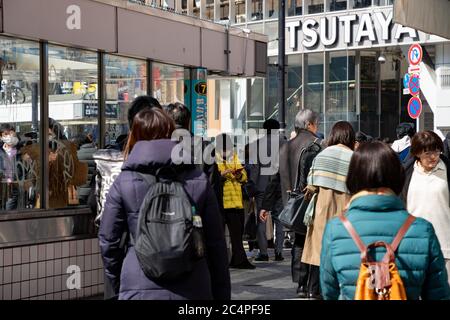 Leute, die auf einem Bürgersteig neben einem Ausgang/Eingang der U-Bahnstation an Shibuya Scramble Kreuzung gehen. Tsutaya Gebäude im Hintergrund. Tokio, Japan. Stockfoto