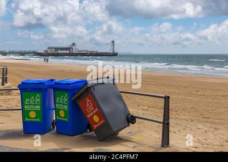Mülltonnen, 2 Recycling- und 1 für allgemeinen Abfall, über den man sich lehnt, an der Promenade in Bournemouth mit Bournemouth Beach und Pier, Dorset UK im Juni Stockfoto