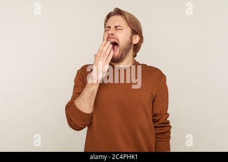 Porträt von schläfrig müde junge bärtige Mann im Sweatshirt mit weit geöffneten Mund, Gähnen Gefühl müde, Mangel an Energie, brauchen Schlaf und Ruhe. Stockfoto