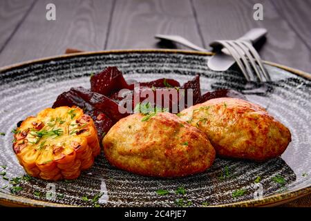 Nahaufnahme von gebratenem Schweineschnitzel mit gerösteten Rote-Bete-Scheiben und gegrilltem Mais auf dunklem Holztisch Stockfoto