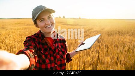Frau Farmer mit digitalem Tablet macht Selfie auf dem Hintergrund eines Weizenfeldes. Stockfoto