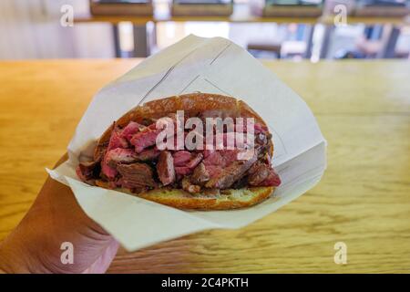 Ausgewählte Konzentration auf geschnittenes mittelseltenes Rindersteak-Sandwich auf der Hand. Stockfoto