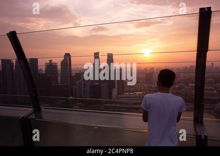 Junger Mann, der den Sonnenuntergang über der Skyline von Singapurs Innenstadt von Marina Bay Sands aus betrachtet beobachtet. Singapur Stockfoto