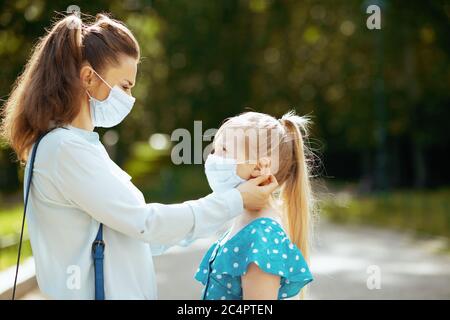 Leben während covid-19 Pandemie. Stilvolle Mutter und Tochter im Freien im Stadtpark tragen medizinische Maske. Stockfoto
