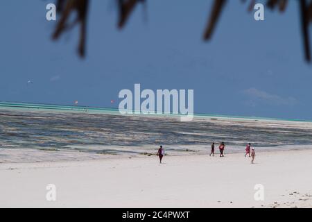 Männer und Frauen, die am Strand in Jambiani, von einer Strohhütte aus gesehen, in Sansibar, Tansania, spazieren Stockfoto