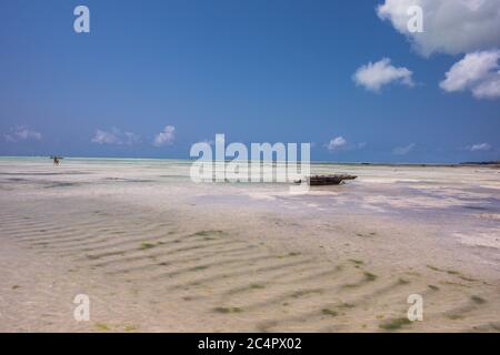 Eine hölzerne Dhow, die bei Ebbe vor dem Strand von Jambiani in Sansibar, Tansania, vor einem klaren blauen Himmel im Wasser sitzt Stockfoto