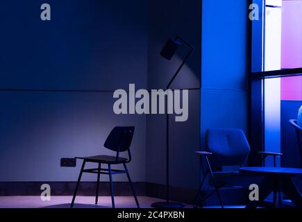 Moderne Sessel und Möbel an einer Fensterwand mit Neonlicht. Stockfoto
