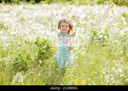 Nettes kleines Mädchen lächelt Sommer auf dem Feld hält eine Windmühle Stockfoto