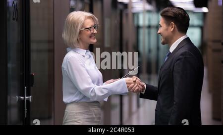Ältere Geschäftsfrau und Geschäftsmann schüttelt sich die Hände stehen im Büroflur Stockfoto