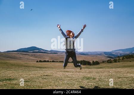 Frau springt auf einem Feld am Berg Stockfoto