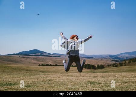 Frau springt auf einem Feld am Berg Stockfoto