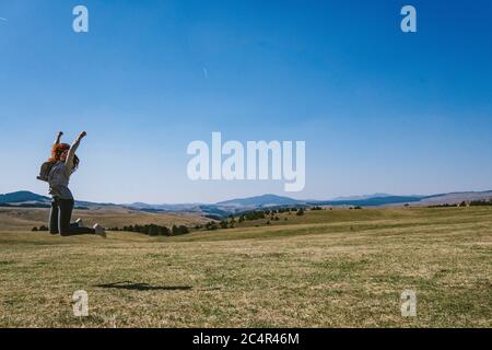 Frau springt auf einem Feld am Berg Stockfoto