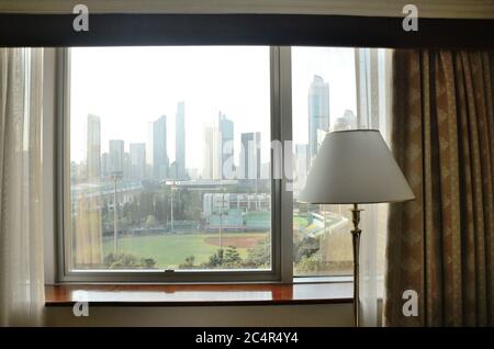 Hotelzimmer in Guangzhou, China. Großes Fenster mit Lampe. Allgemeine Ansicht der Stadt, Stadtbild des TianHe Bezirks mit TianHe Stadion. Stockfoto