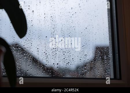 Dunkles Regenwetter mit grauem Himmel und vielen Regentropfen auf der Fensterscheibe. Stockfoto