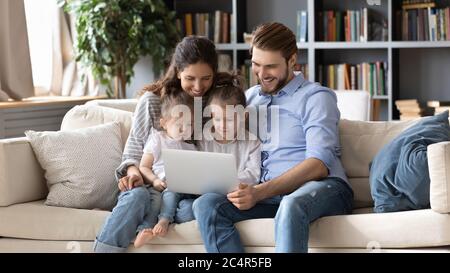 Glückliche Eltern mit zwei kleinen Töchtern, die zusammen einen Laptop benutzen Stockfoto