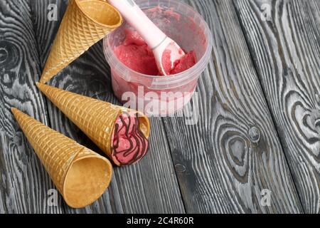 Erdbeereis in einem Waffelkegel. Garniert mit Schokolade. In der Nähe gibt es leere Waffelkegel ohne Eis. Eisbehälter und Löffel. Auf pi Stockfoto