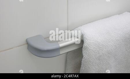 Weißes Handtuch hängt auf einem Aluminium-Handtuchhalter mit einer Wand aus weißem Keramik Hintergrund Stockfoto