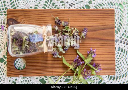 Zusammensetzung von Prunella vulgaris (bekannt als gemeinsame selbst-heilen, heilen-alle, Wundwort trockenen Kräuterteepulver mit frischen Blumen auf natürlichem Holz. Stockfoto