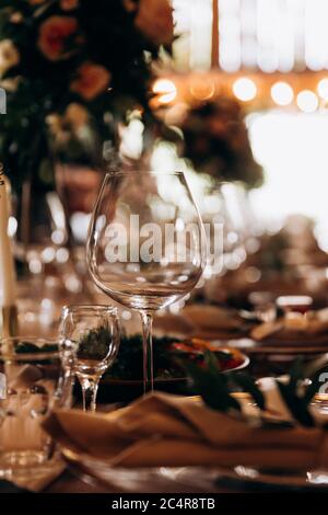 Nahaufnahme der Hochzeitstisch mit glänzenden Weinglas und schöne Dekoration. Blumenarrangements und Kerzen herum. Moderne Bedienung für Feiern. Stockfoto
