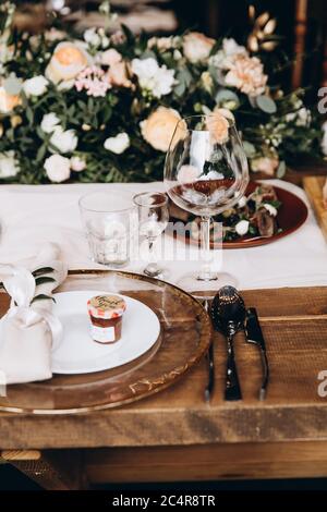 Hochzeitstisch mit Tellern, Messern, Gabeln, Gläsern und bunten Blumen dekoriert. Trendige Einrichtung im rustikalen Stil. Konzept der Tabelleneinstellungen und Flo Stockfoto