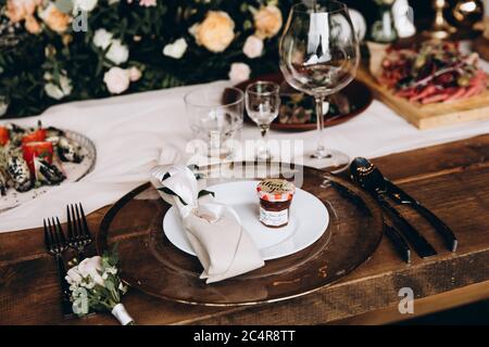 Nahaufnahme der Hochzeitsdetails auf festlichen Holztischen mit Tellern, Besteck und Gläsern. Blumensträuße schmücken alles um. Stilvolle Einrichtung und Kombis Stockfoto