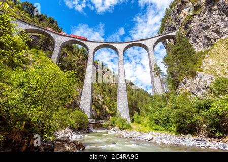 Landwasser Viadukt über Fluss, Filisur, Schweiz. Es ist Wahrzeichen der Schweizer Alpen. Rote Bahn fährt auf hoher Eisenbahnbrücke in den Bergen. Landschaftlich schöner Blick auf Stockfoto
