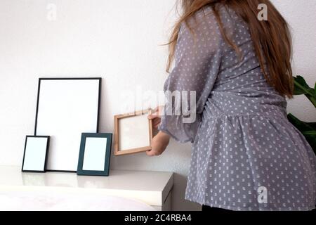 Frau hält leere Foto oder Bilderrahmen in einem modernen Raum in der Nähe der weißen Wand, skandinavisches Design, Retro-Interieur Stockfoto