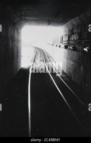 Feine Schwarz-Weiß-Fotografie der 70er Jahre von Eisenbahnschienen, die zum Licht am Ende des Tunnels führen. Stockfoto