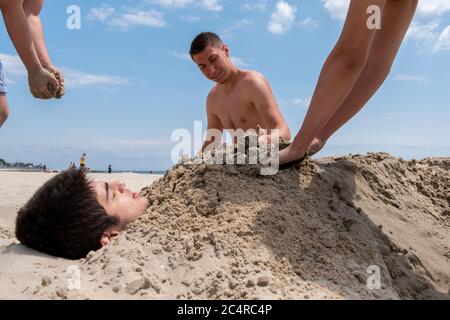 Der kleine Junge wird von seinen Freunden am Strand in İstanbul im Sand begraben. Im Sand begraben. Stockfoto